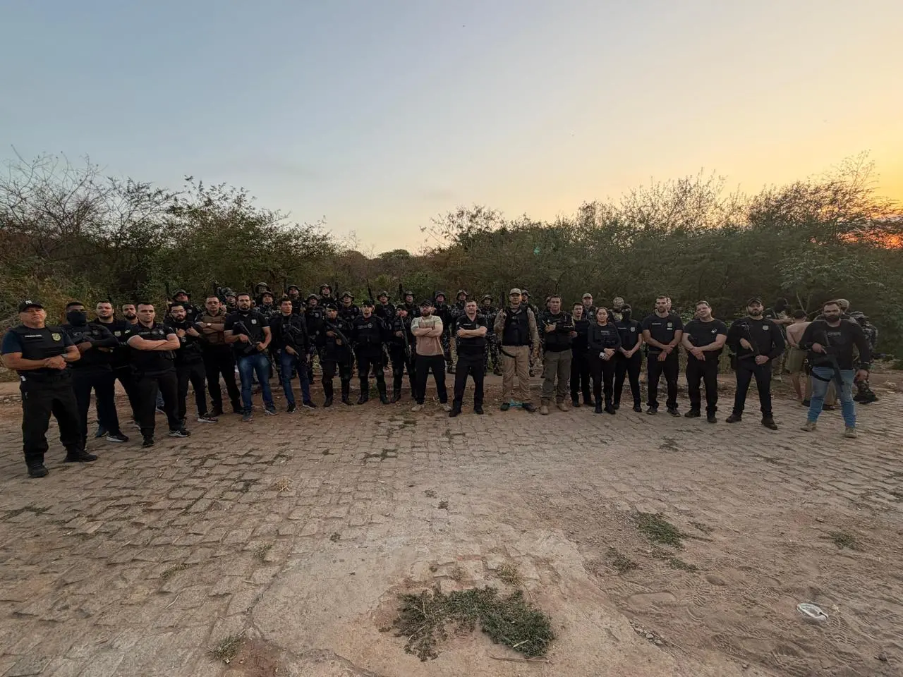 Foto mostra grupo de policiais militares e civis fardados posando para câmera, ao amanhecer, com vegetação de caatinga atrás. Eles participaram da prisão de um homem suspeito de homicídio no Ceará.