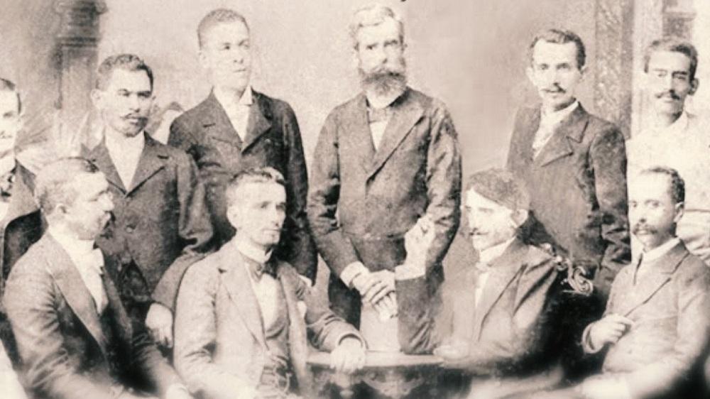 Imagem antiga mostra integrantes da Padaria Espiritual, movimento cultural cearense do século XIX. Imagem mostra dez homens de paletó, sendo seis em pé e outros quatro sentados.