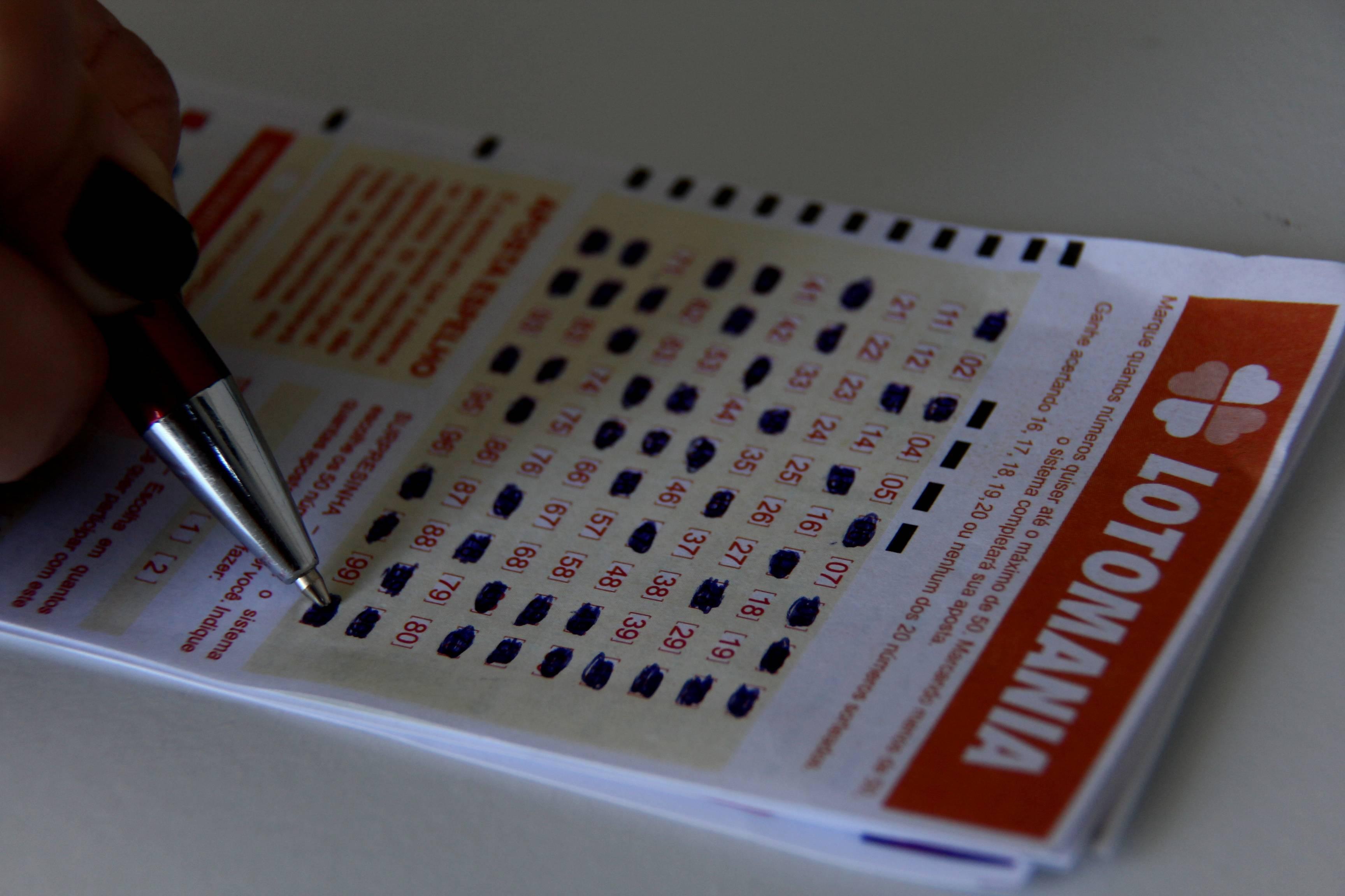 Imagem mostra mão de uma pessoa preenchendo um bilhete da Lotomania com uma caneta.