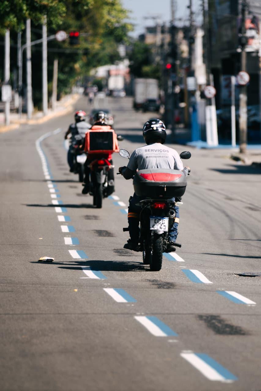 Motociclistas trafegam por faixa azul em avenida de Fortaleza.