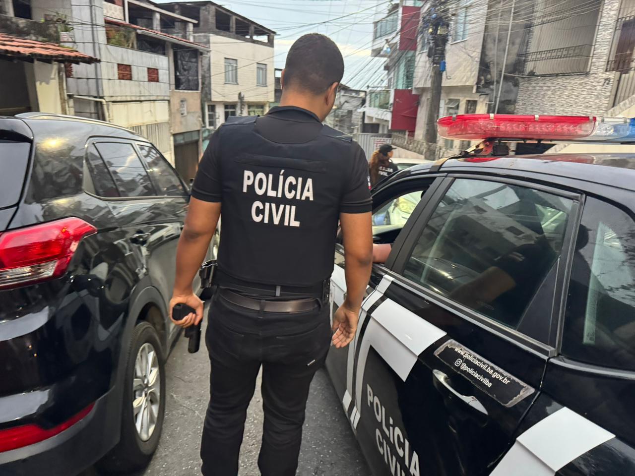 imagem mostra policial civil, de costas, entre viaturas, em rua de salvador durante operação contra o CV na bahia e no ceará.