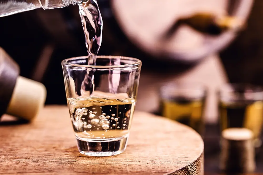 Bebida alcoólica destilada sendo colocada em copo de vidro em cima de mesa de madeira.