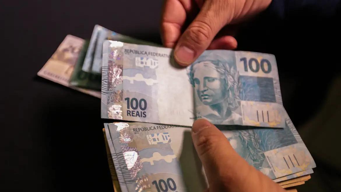 Closa nas mãos de uma pessoa branca que segura um leque de dinheiro.