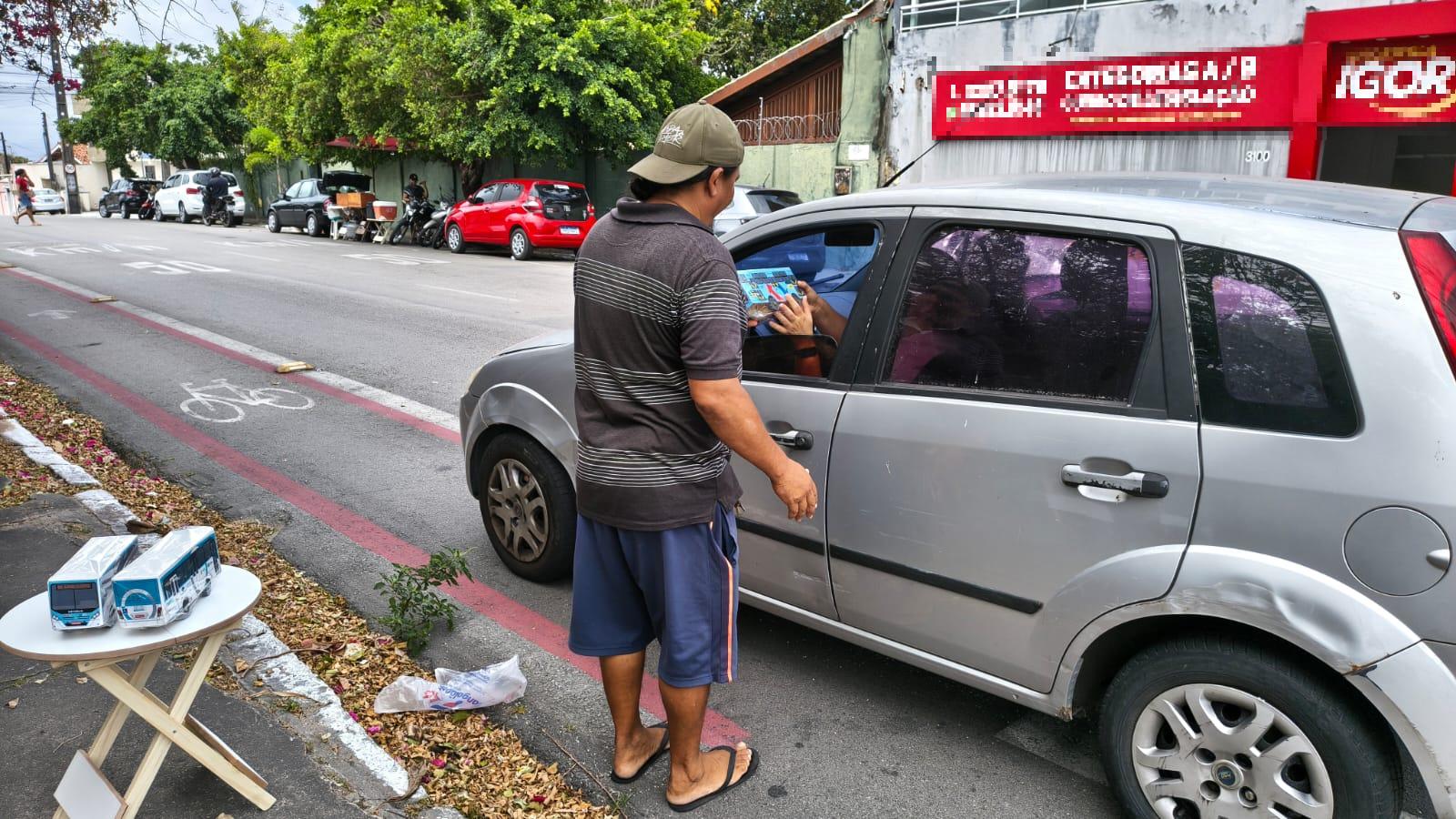 Homem entregando ônibus de madeira para motorista de carro.