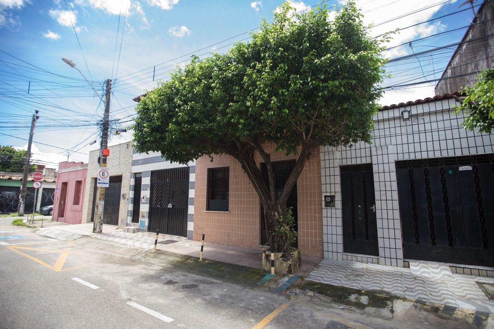 Imagem mostra fachadas de diversas casas em rua tranquila do Centro de Fortaleza. Na calçada, uma grande árvore se ergue.