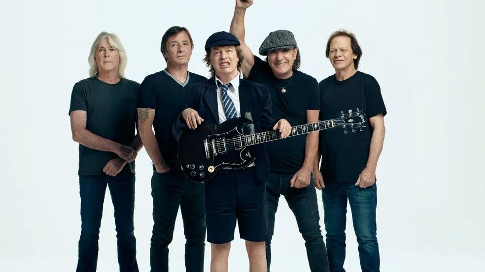 Imagem mostra banda de rock AC/DC usando roupas em tons escuros sobre fundo branco.