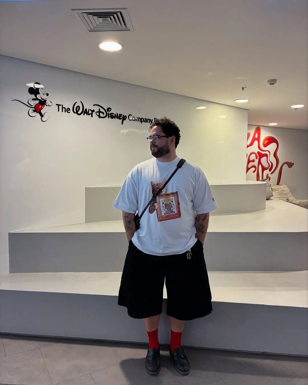 Imagem do médico Vitor Arruda de camisa branca com uma estampa e uma bolsa a tiracolo.