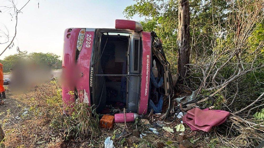 Ônibus tombado em uma zona de mata. Ao lado do veículo, pertences pessoais de passageiros.