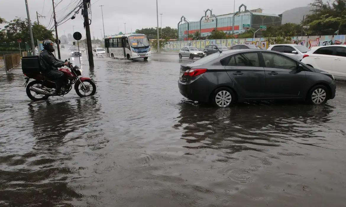 Um carro e uma moto tentam se locomover em uma avenida inundada após chuvas na cidade do Rio de Janeiro.