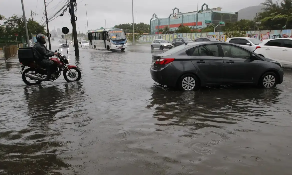 Um carro e uma moto tentam se locomover em uma avenida inundada após chuvas na cidade do Rio de Janeiro.