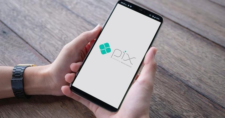 Imagem de uma mão com um celular e a inscrição pix.