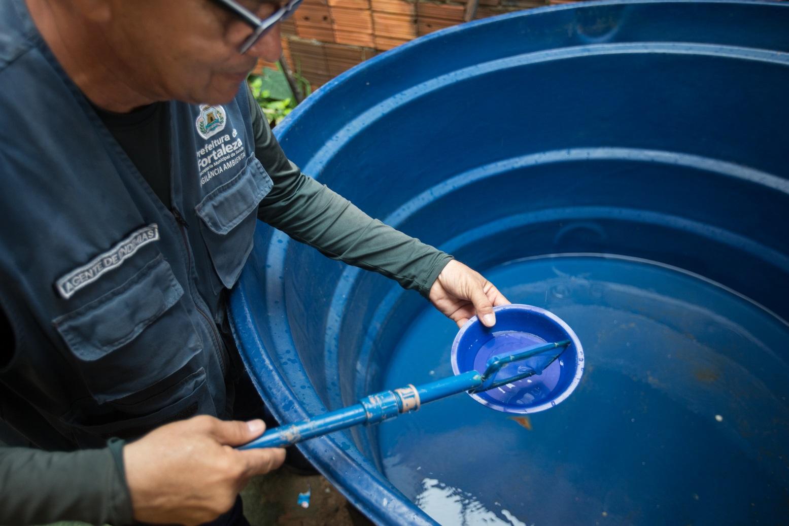 Um agente de endemias da Prefeitura de Fortaleza coleta amostras de água em um reservatório azul, durante inspeção de rotina para combate ao mosquito Aedes aegypti.