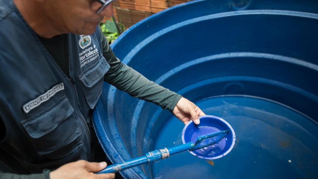 Um agente de endemias da Prefeitura de Fortaleza coleta amostras de água em um reservatório azul, durante inspeção de rotina para combate ao mosquito Aedes aegypti.