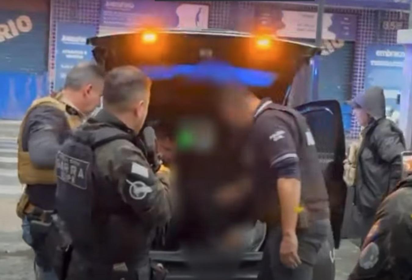 A foto mostra policiais civis realizando a escolta de um suspeito preso, saindo da viatura policial, em São Paulo.