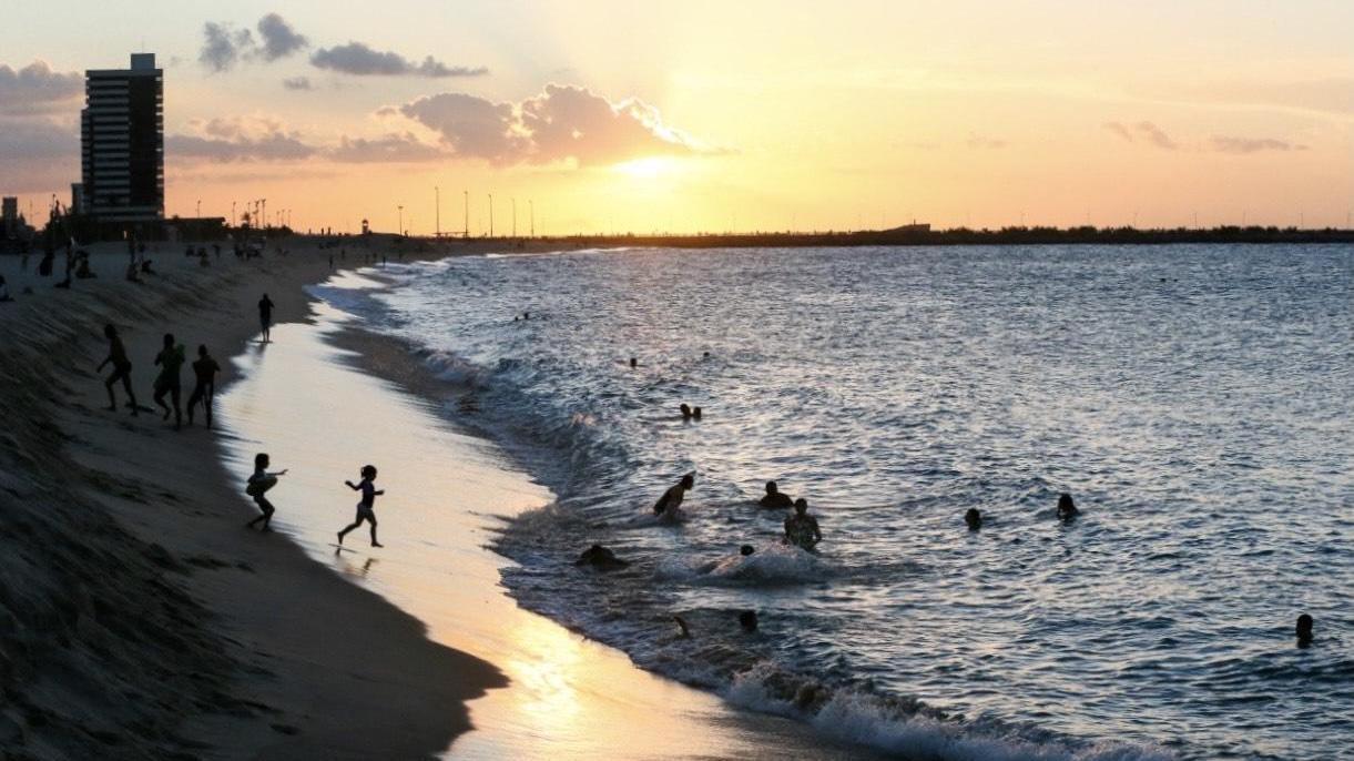 Por do sol na praia com banhista tomando banho de  mar.