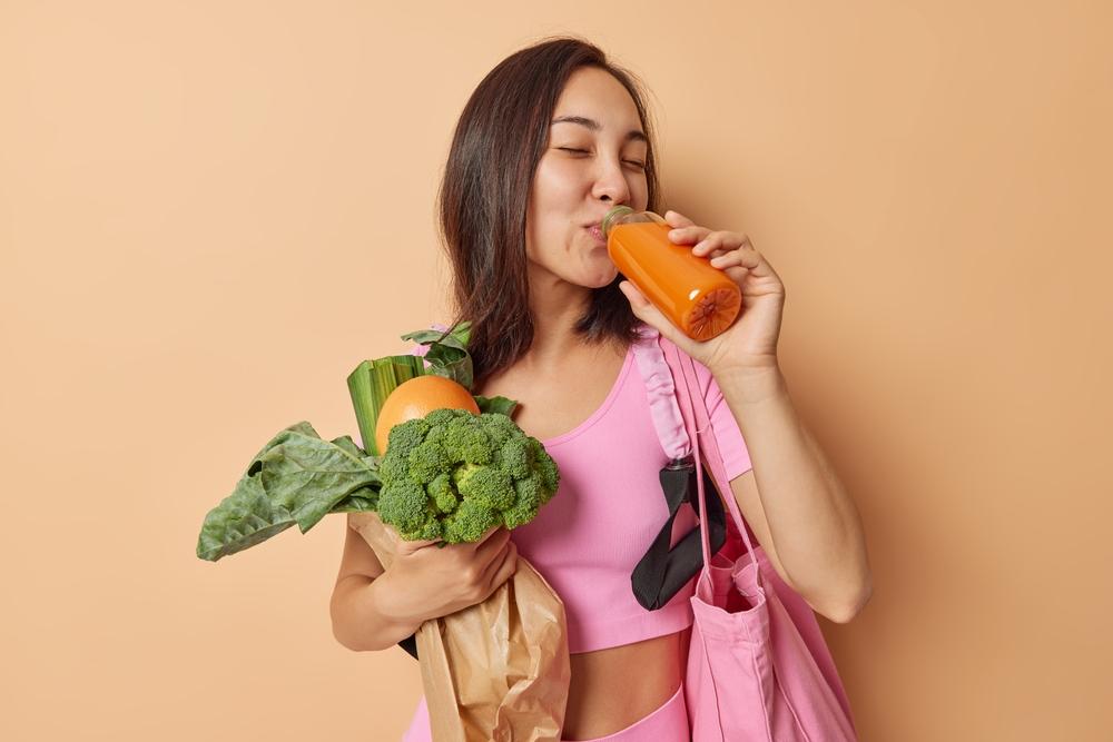 foto de mulher segurando vegetais verde-escuros na mão, tomando suco de frutas cítricas. Imagem para ilustrar matéria sobre alimentos que ajudam a espantar o mau humor.