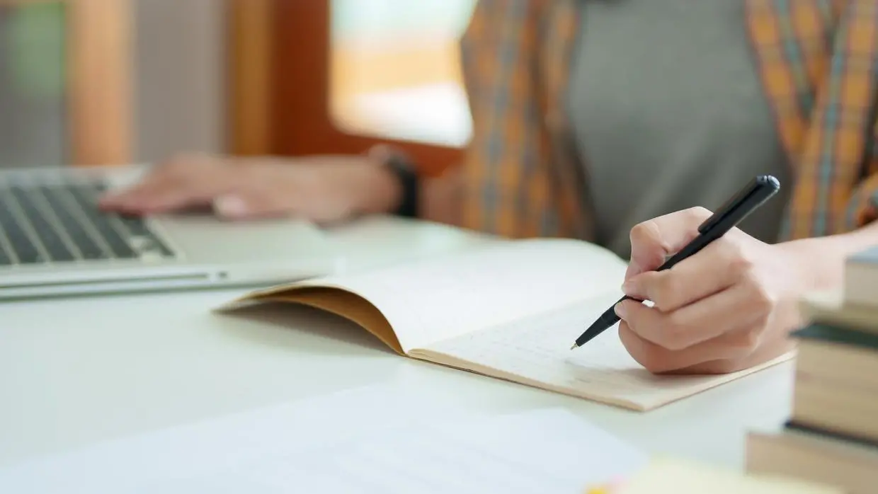 foto de aluno escrevendo em caderno com caneta preta.