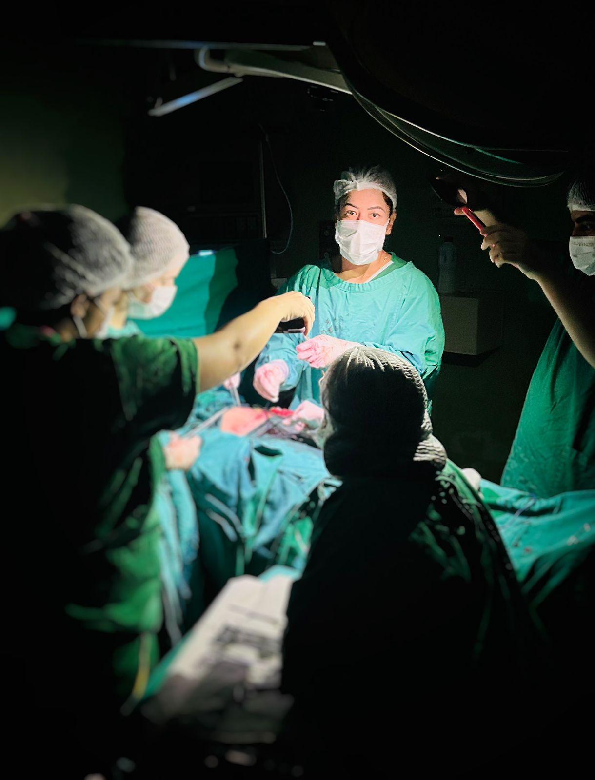Equipe médica realiza cesárea em meio à falta de luz, com lanternas do celular iluminando o campo cirúrgico.