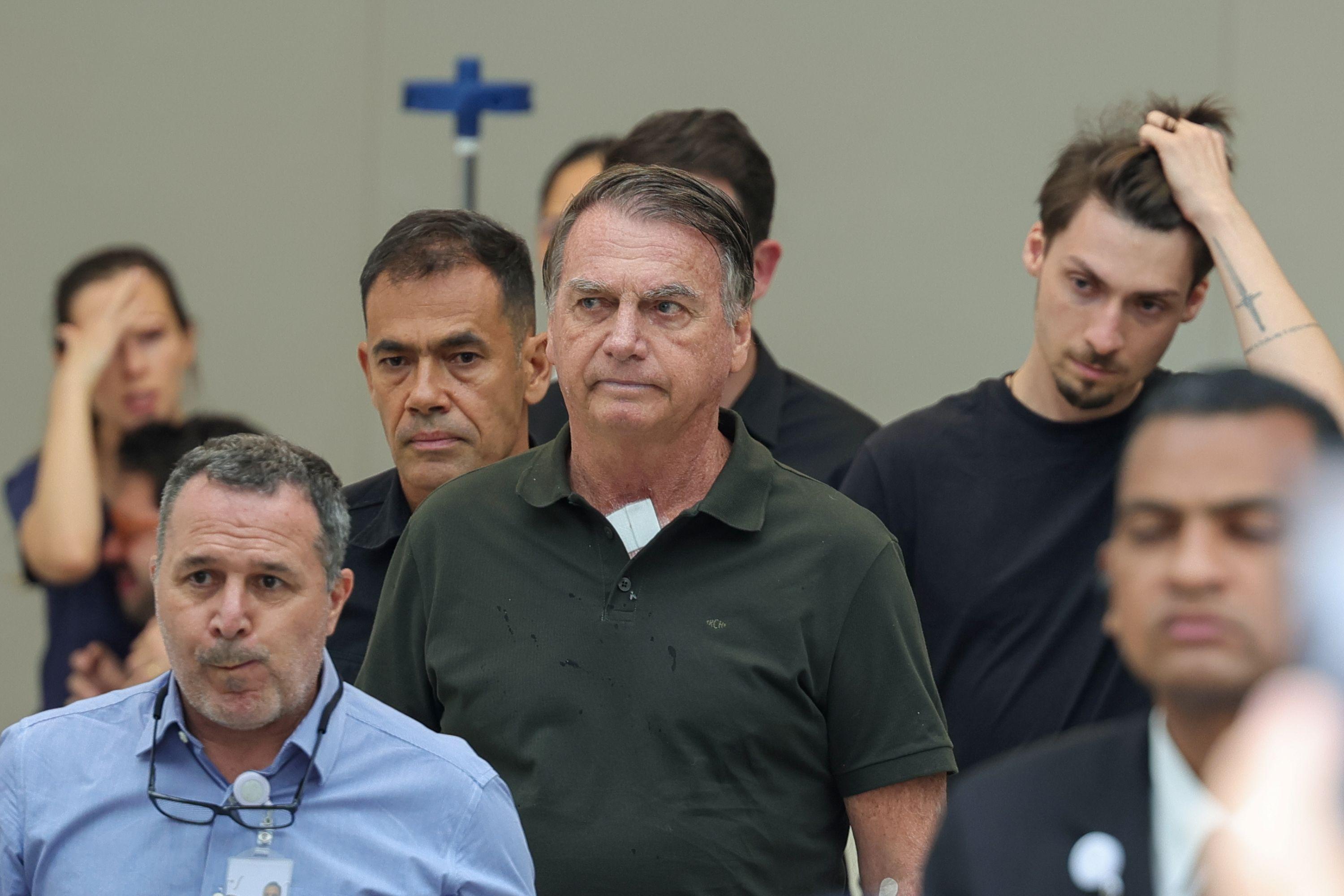 Imagem mostra Jair Bolsonaro, ex-presidente do Brasil, olhando para o lado. ele está cercado por outros homens.