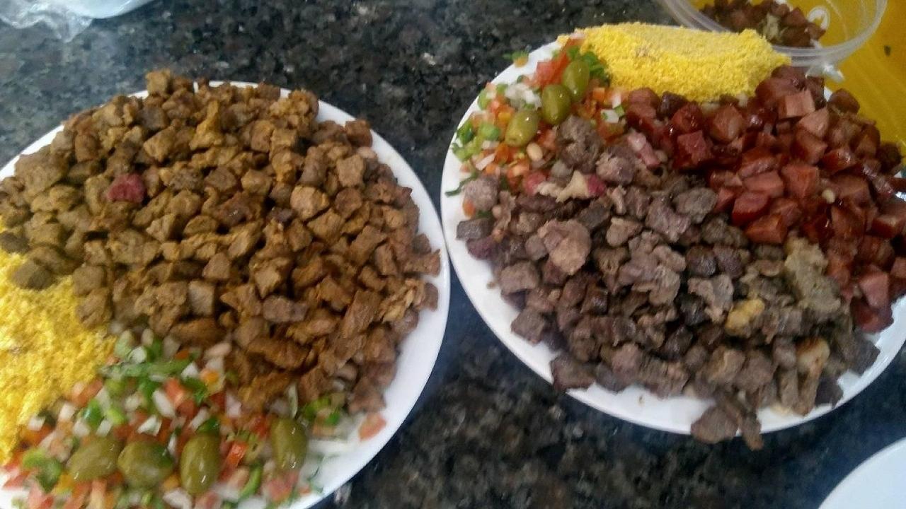 Dois pratos com Arrumadinho nordestino. Cada prato contém carne de sol em cubos, farofa amarela e vinagrete. O prato da direita também inclui linguiça ou charque frito.