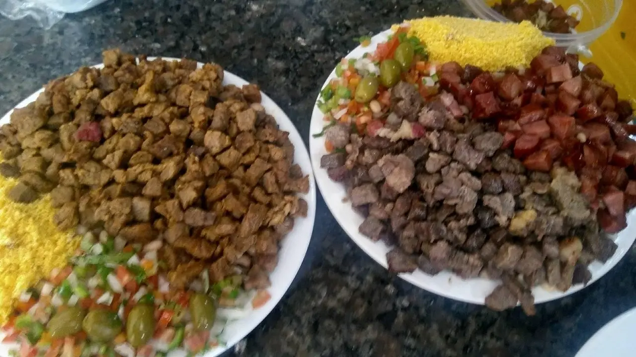 Dois pratos com Arrumadinho nordestino. Cada prato contém carne de sol em cubos, farofa amarela e vinagrete. O prato da direita também inclui linguiça ou charque frito.