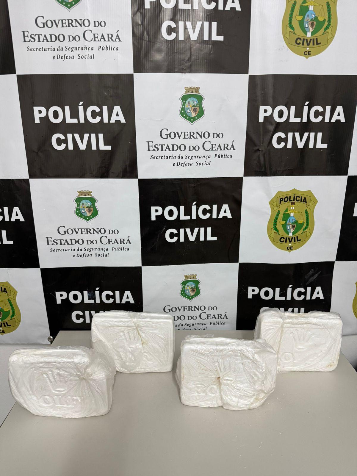 Imagem mostra quatro pacotes de cocaína, em formato de tijolos brancos, dispostos sobre uma mesa com o logo da Polícia Civil e do Governo do Ceará ao fundo.