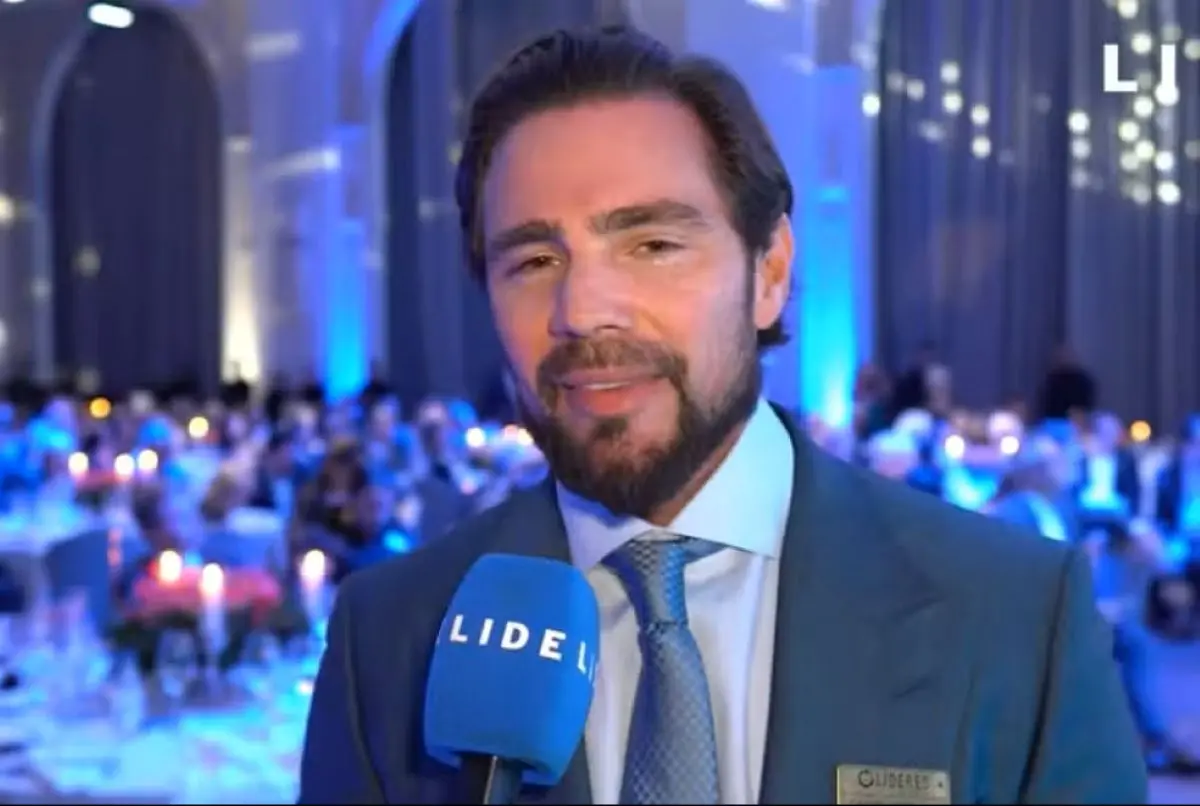 Foto de Daniel Vorcaro, de terno e gravata azul, falando em um microfone azul.