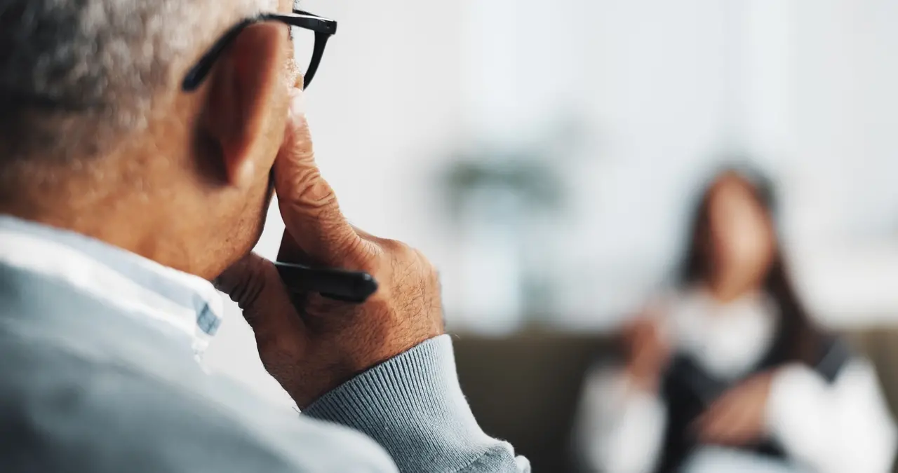Foto mostra homem com mão na face enquanto escuta mulher falando ao fundo.