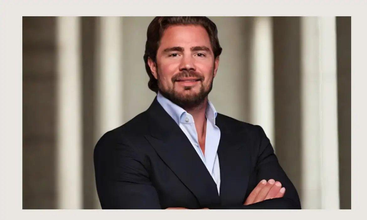 Imagem mostra banqueiro Daniel Vorcaro, dono Banco Master, usando terno e posando para foto de braços cruzados e sorrindo.