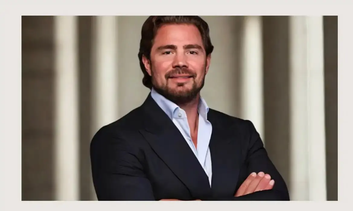 Imagem mostra banqueiro Daniel Vorcaro, dono Banco Master, usando terno e posando para foto de braços cruzados e sorrindo.