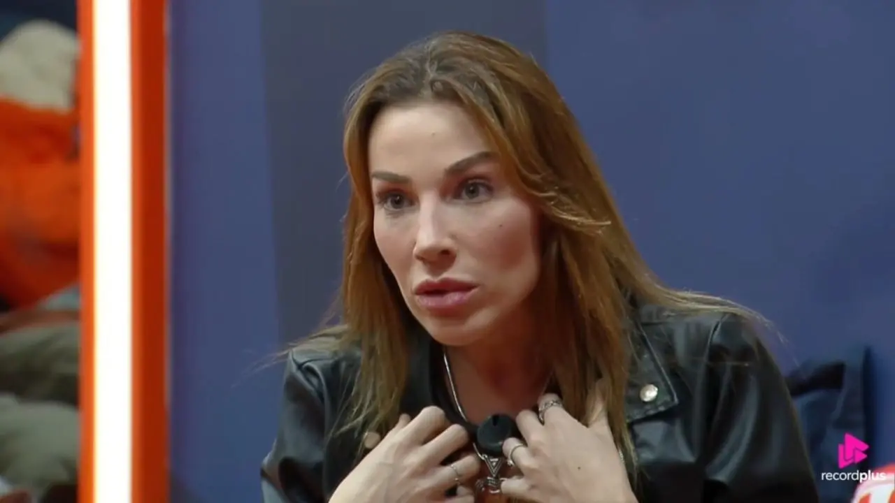 Maria Caporusso é uma mulher branca de cabelo acobreado. Na foto, ela está debatendo com uma pessoa.