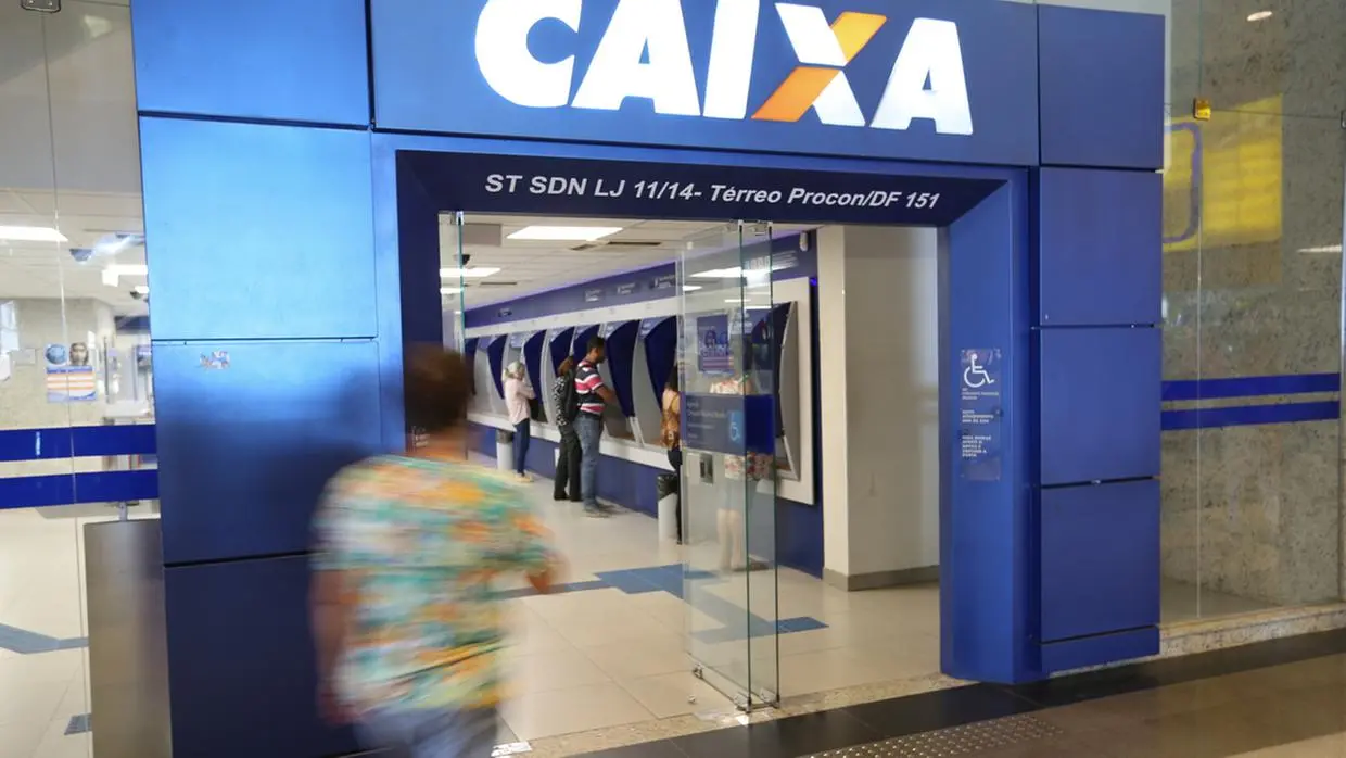 Imagem de uma agência da Caixa Econômica Federal, com fila de clientes e caixas eletrônicos disponíveis.