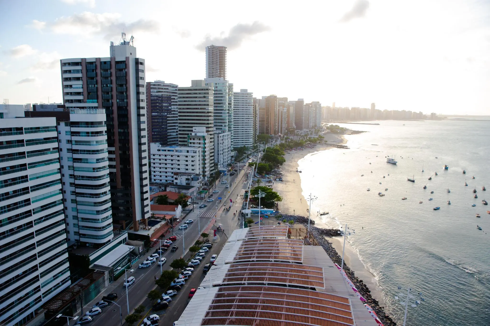 Imagem aérea da orla da Beira Mar, em Fortaleza. À esquerda, prédios. À direita, o mar.