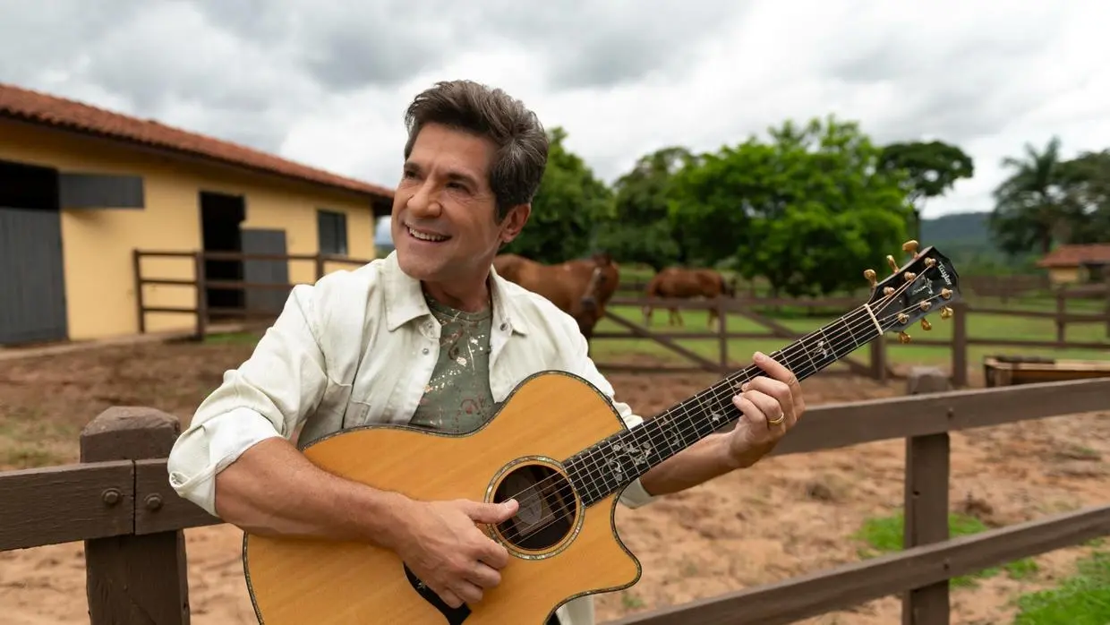 foto do cantor Daniel tocando violão em frente à fazenda.