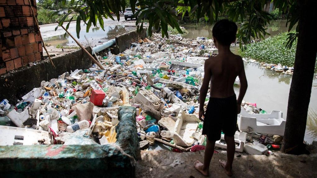 Imagem mostra menino diante de rio totalmente poluído por lixo em Fortaleza.