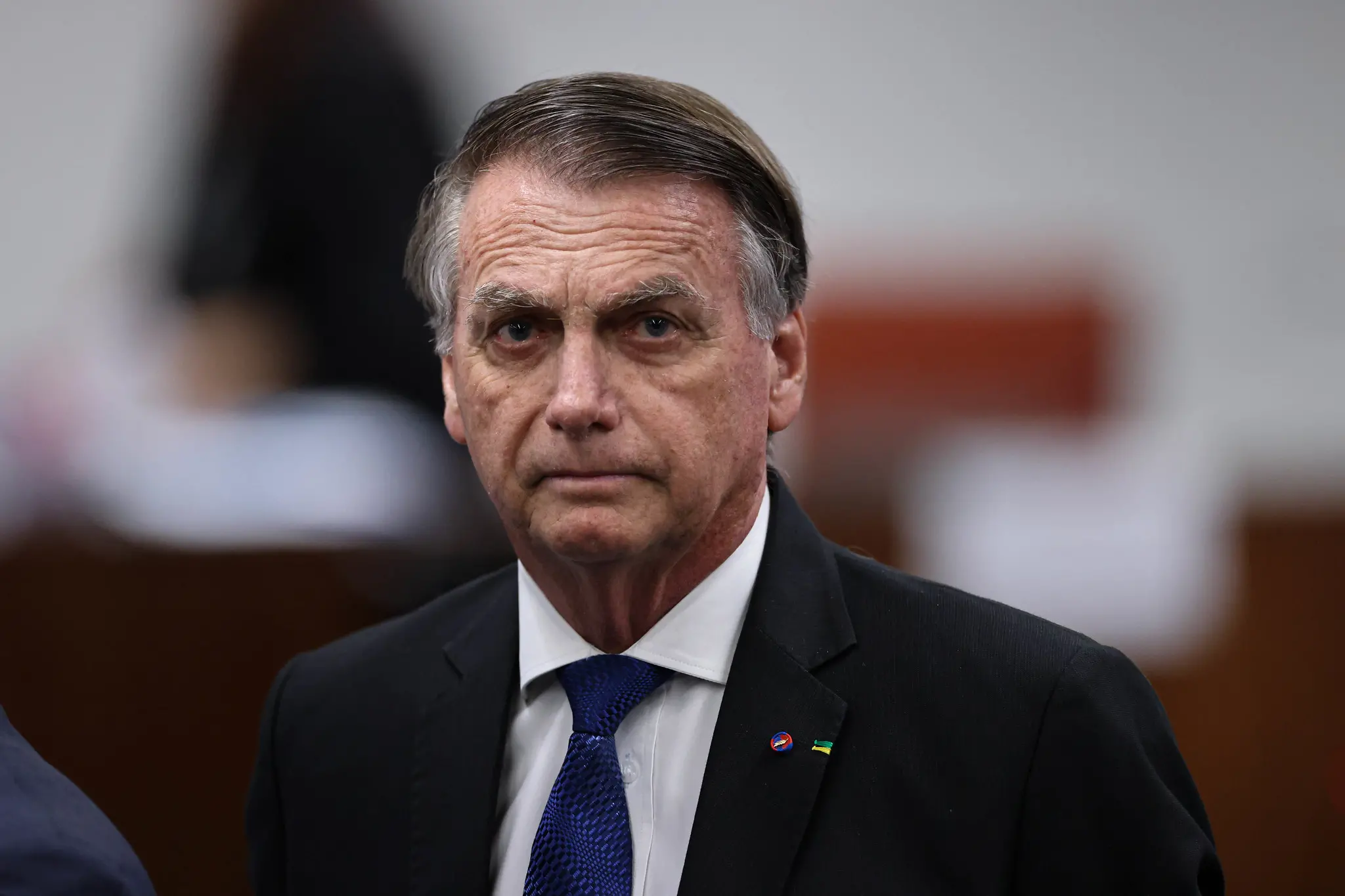 A imagem mostra o ex-presidente Jair Bolsonaro, de terno e gravata, durante um depoimento ao STF, com pessoas ao fundo.