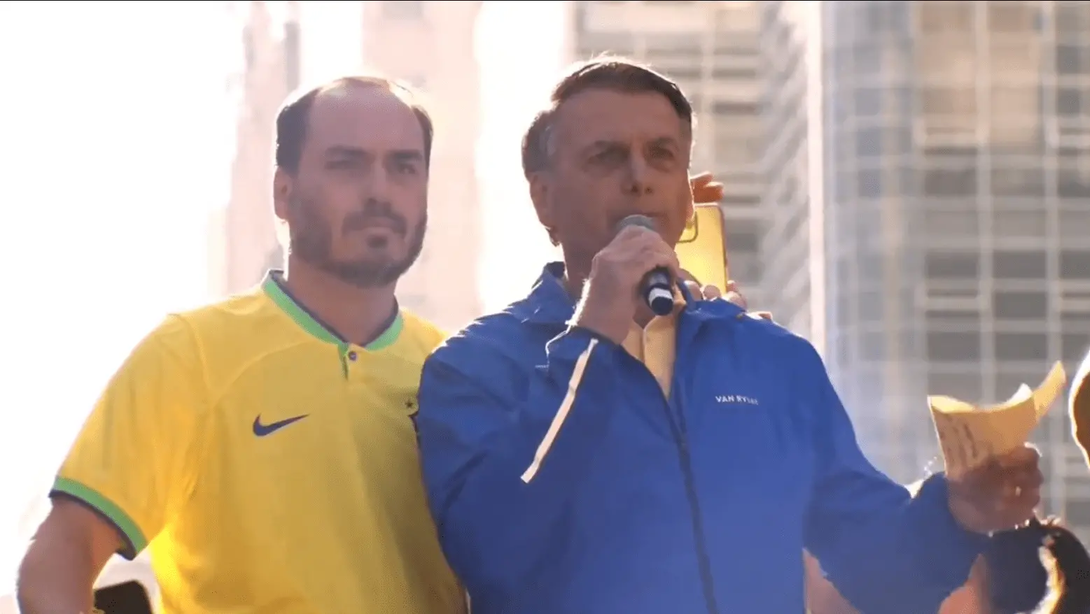 Carlos Bolsonaro ao lado do pai, o ex-presidente Jair Bolsonaro, em comício na Avenida Paulista. Eles estão em cima de trio elétrico.