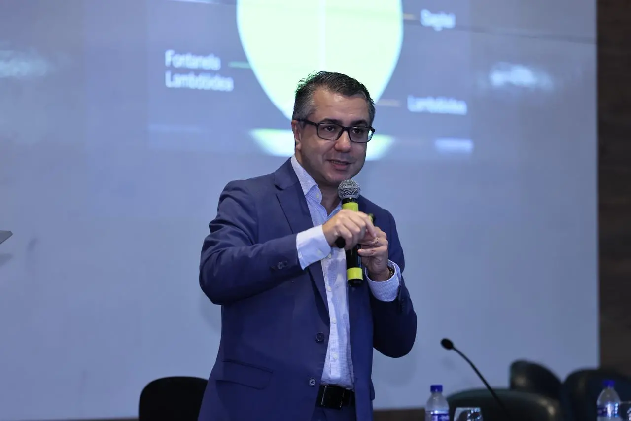 Eduardo Jucá palestra durante simpósio. Ele usa terno cinza e camisa social branca.