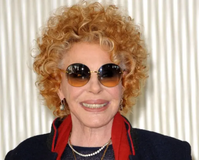 Ornella Vanoni era uma mulher idosa de cabelo loiro. Na foto, ela está sorrindo e usa óculos escuros.