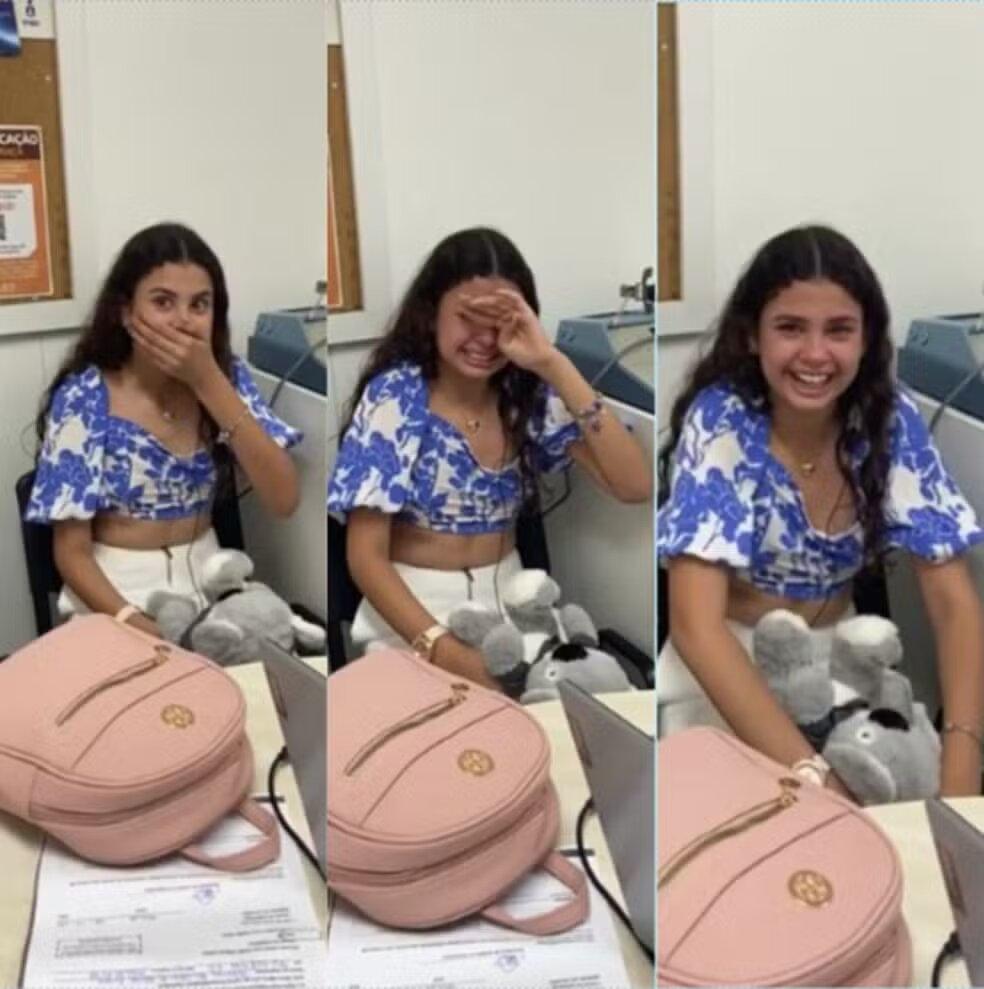 Na imagem, uma montagem de três fotos mostra uma jovem, Laís Vitória, sentada em uma mesa, reagindo com emoção. Ela usa um top branco e azul e calças brancas, com uma mochila rosa e um bicho de pelúcia cinza ao lado de um notebook. Na primeira foto, ela está com a mão sobre a boca, surpresa. Na segunda, ela está emocionada, chorando de alegria, com a mão no rosto. Na terceira foto, ela sorri abertamente, claramente feliz.