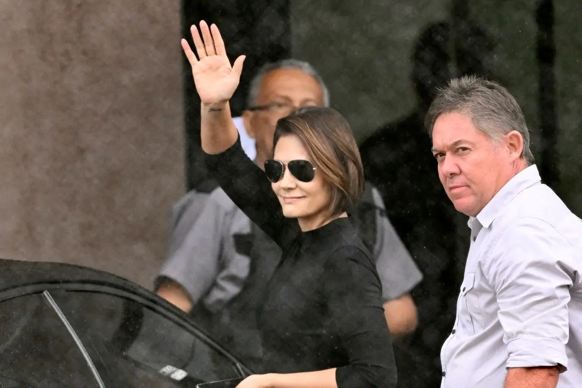Michelle Bolsonaro, esposa do ex-presidente do Brasil (2019–2023) Jair Bolsonaro, acena para apoiadores ao chegar à sede da Polícia Federal, onde Bolsonaro está detido, em Brasília, em 23 de novembro de 2025. Michelle está de roupa preta e óculos escuros.