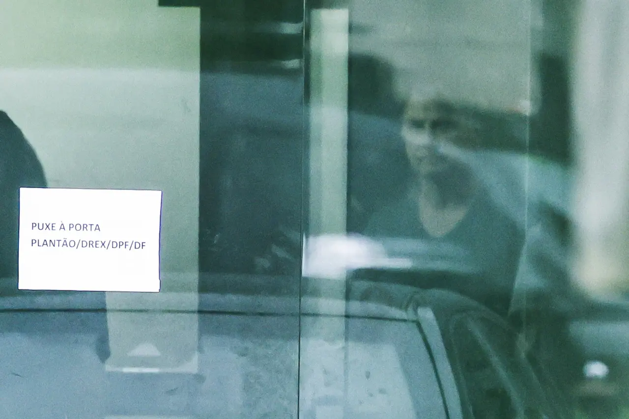 Imagem mostra o ex-presidente Jair Bolsonaro visto através da porta da Superintendência da Polícia Federal, onde está preso, no final da visita da ex-primeira-dama Michelle Bolsonaro (fora do quadro) em Brasília, Brasil, no dia 23 de novembro de 2025.