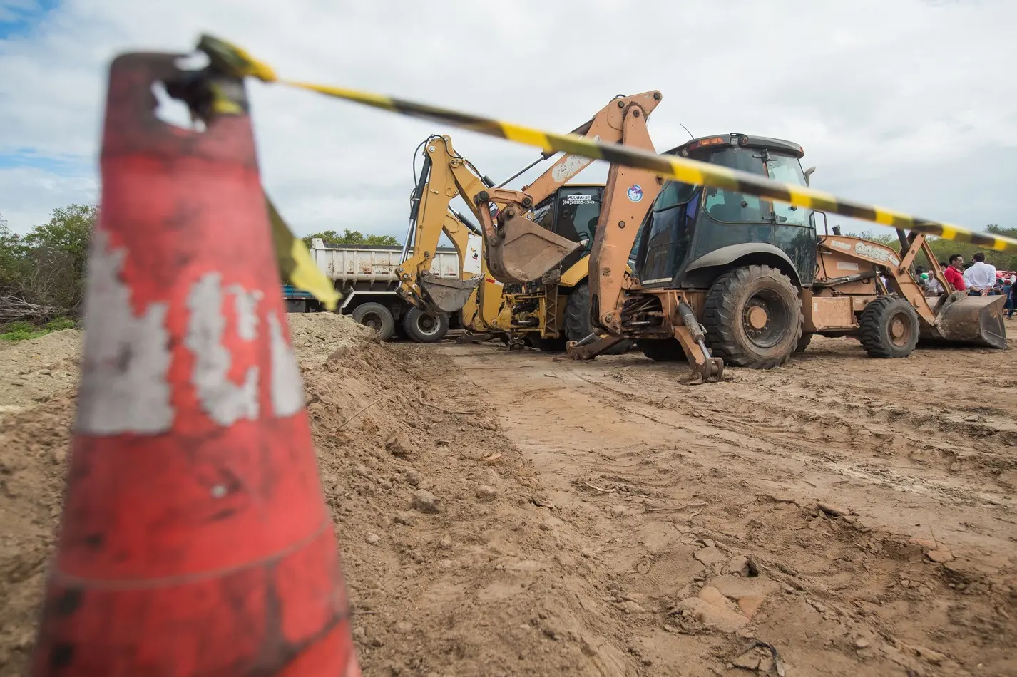 Foto que contém canteiro de obras com trator e cone isolando área.