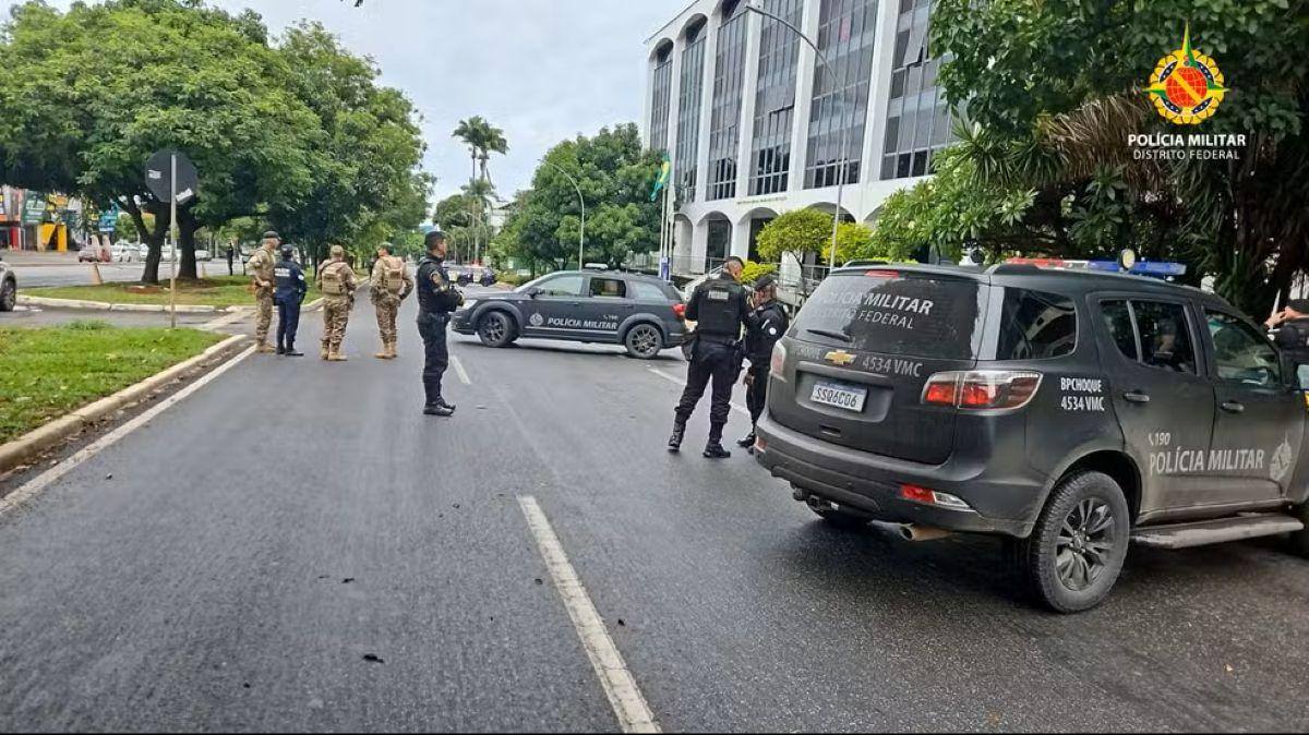 Oficiais da Polícia Militar do Distrito Federal e viaturas em uma rua urbana, em frente a um edifício com colunas, indicando operação de segurança ou bloqueio.