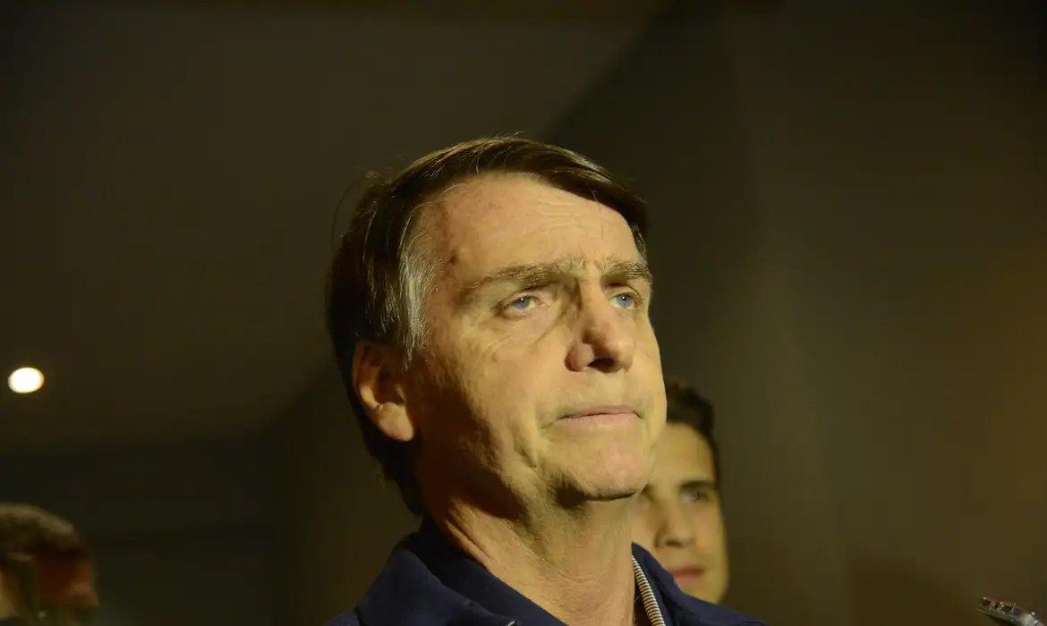 Jair Bolsonaro observa alguma coisa.