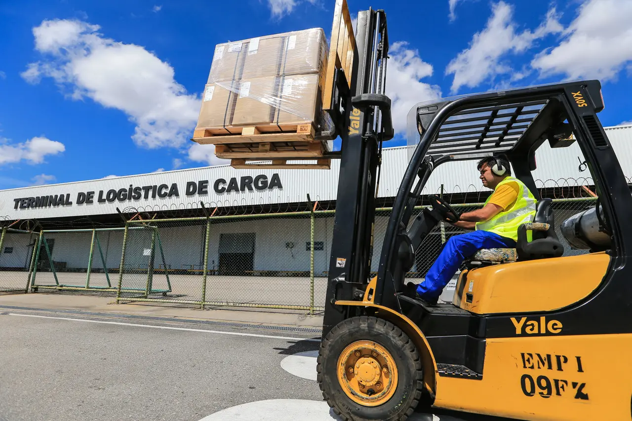 imagem mostra homem manobrando um pequeno caminhão de cargas em frente ao terminal de logística de carga do aeroporto de fortaleza.