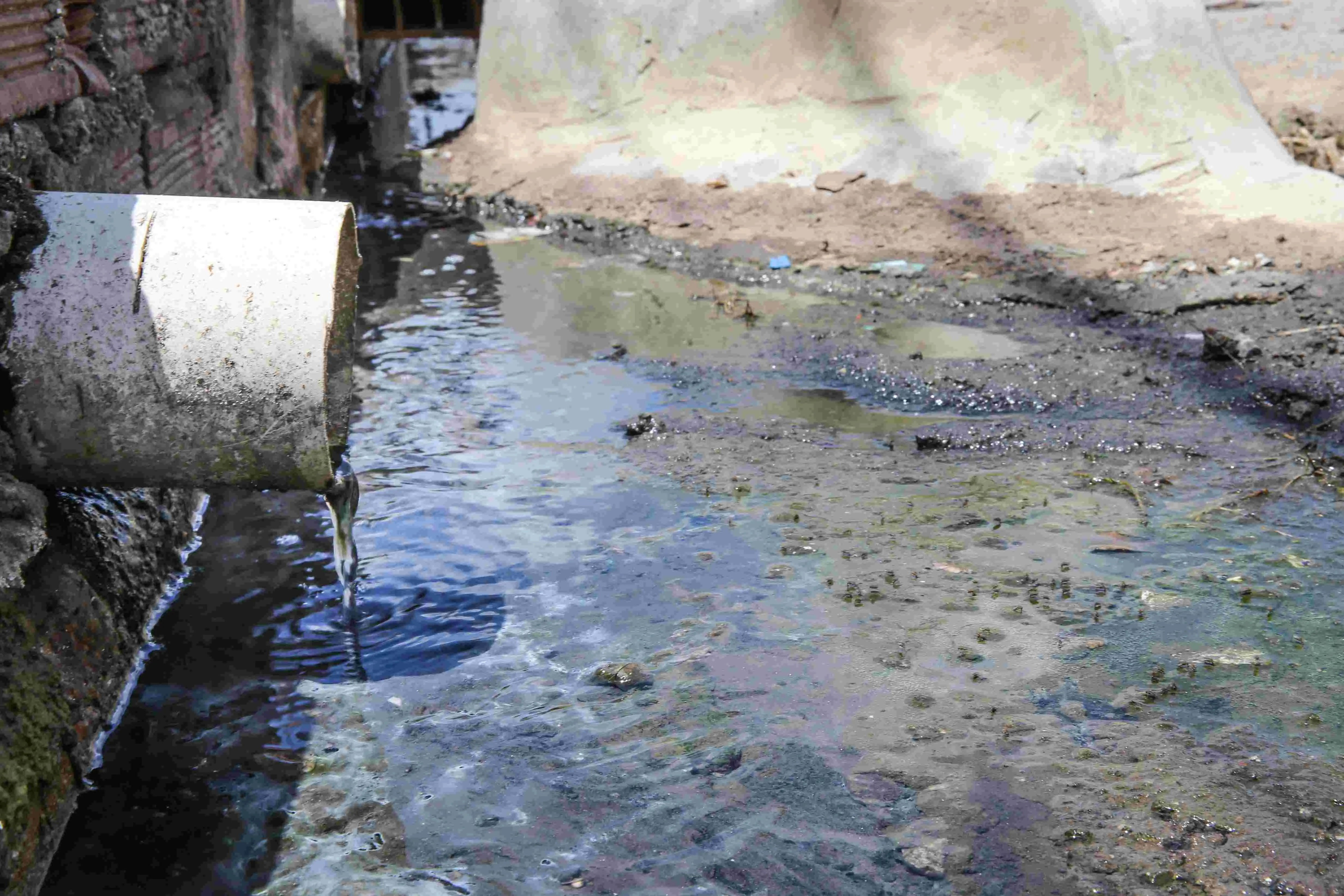 Foto de tubulação branca despejando esgoto no chão de uma rua.