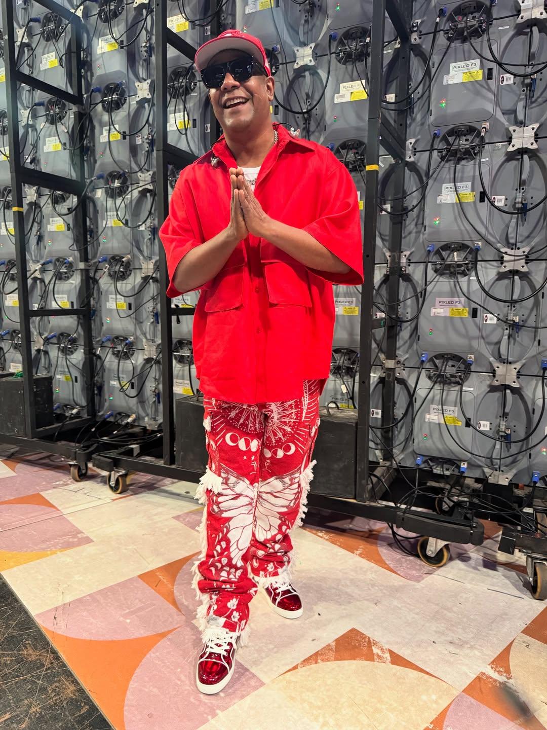 Márcio Victor vestindo camisa vermelha, com boné vermelha, por trás de várias caixas de som.