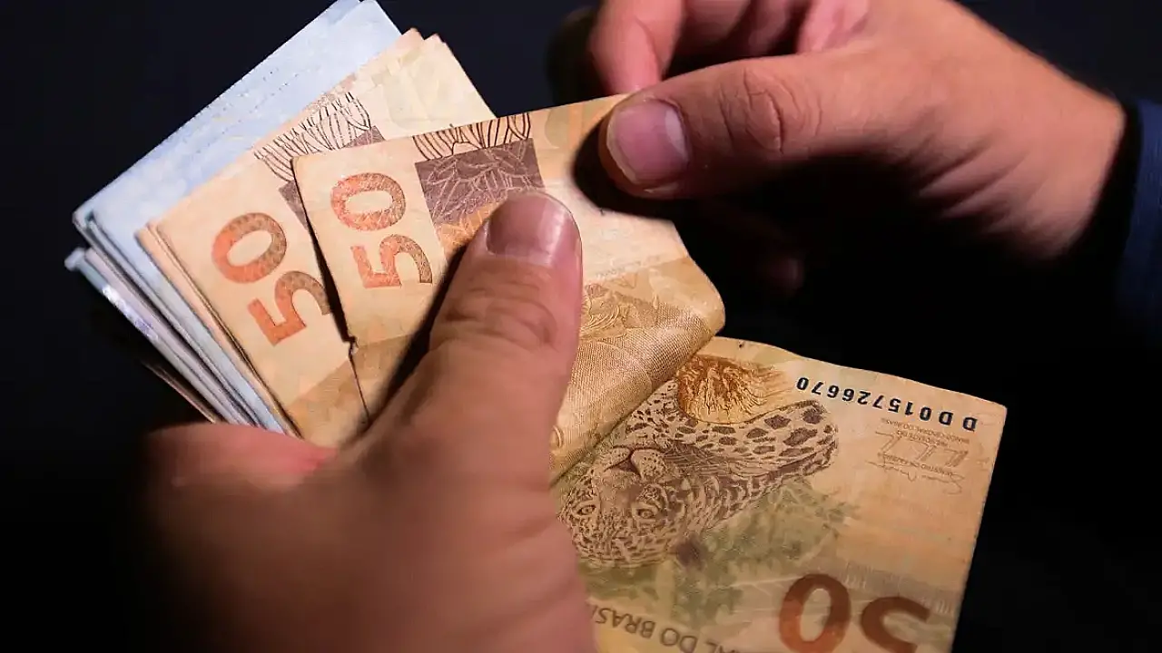 Mão com cédulas com notas R$ 100 e R$ 50 contando o dinheiro.