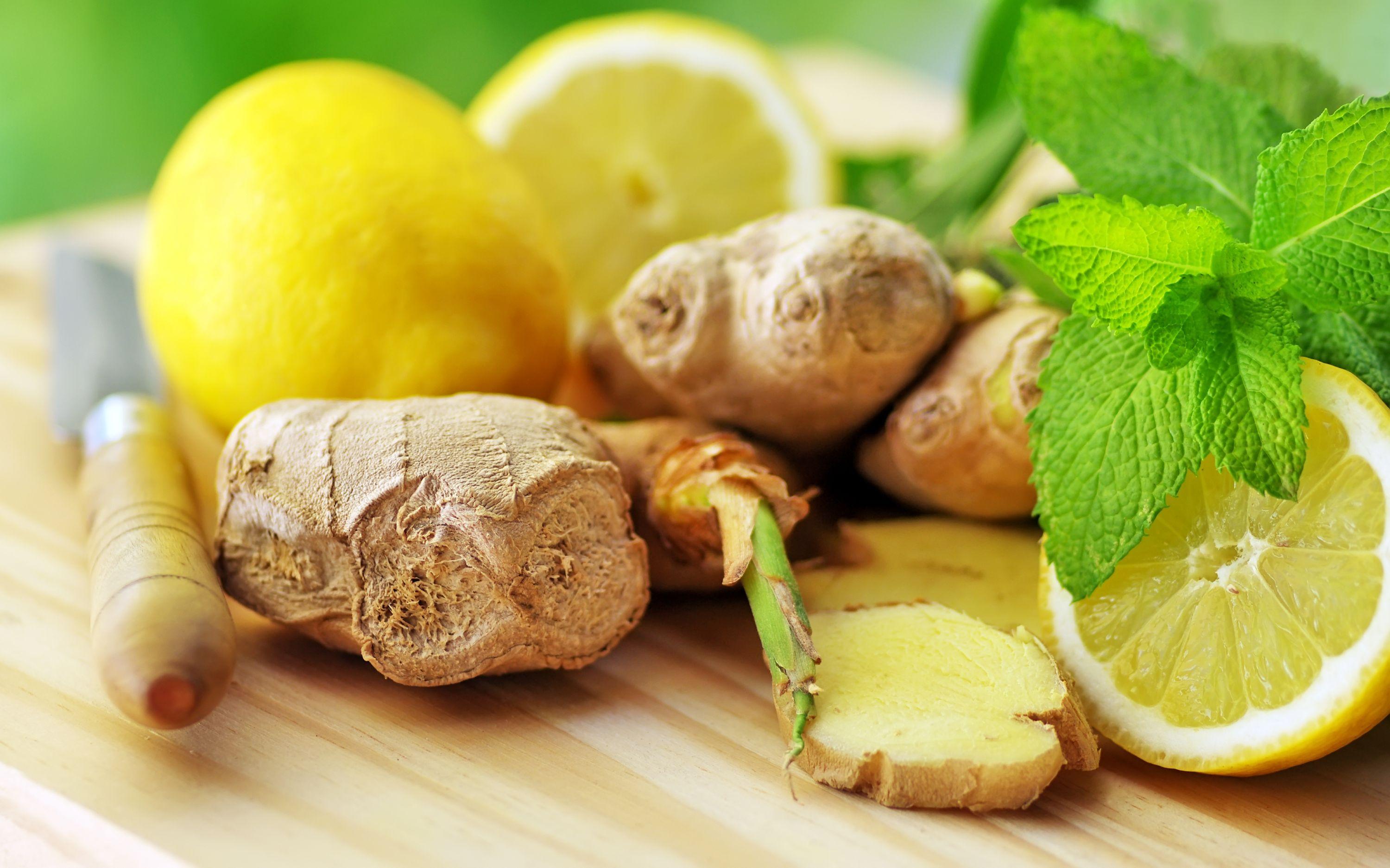 Gengibre, limões frescos e folhas de hortelã sobre uma tábua de corte de madeira, com um cabo de faca à vista.